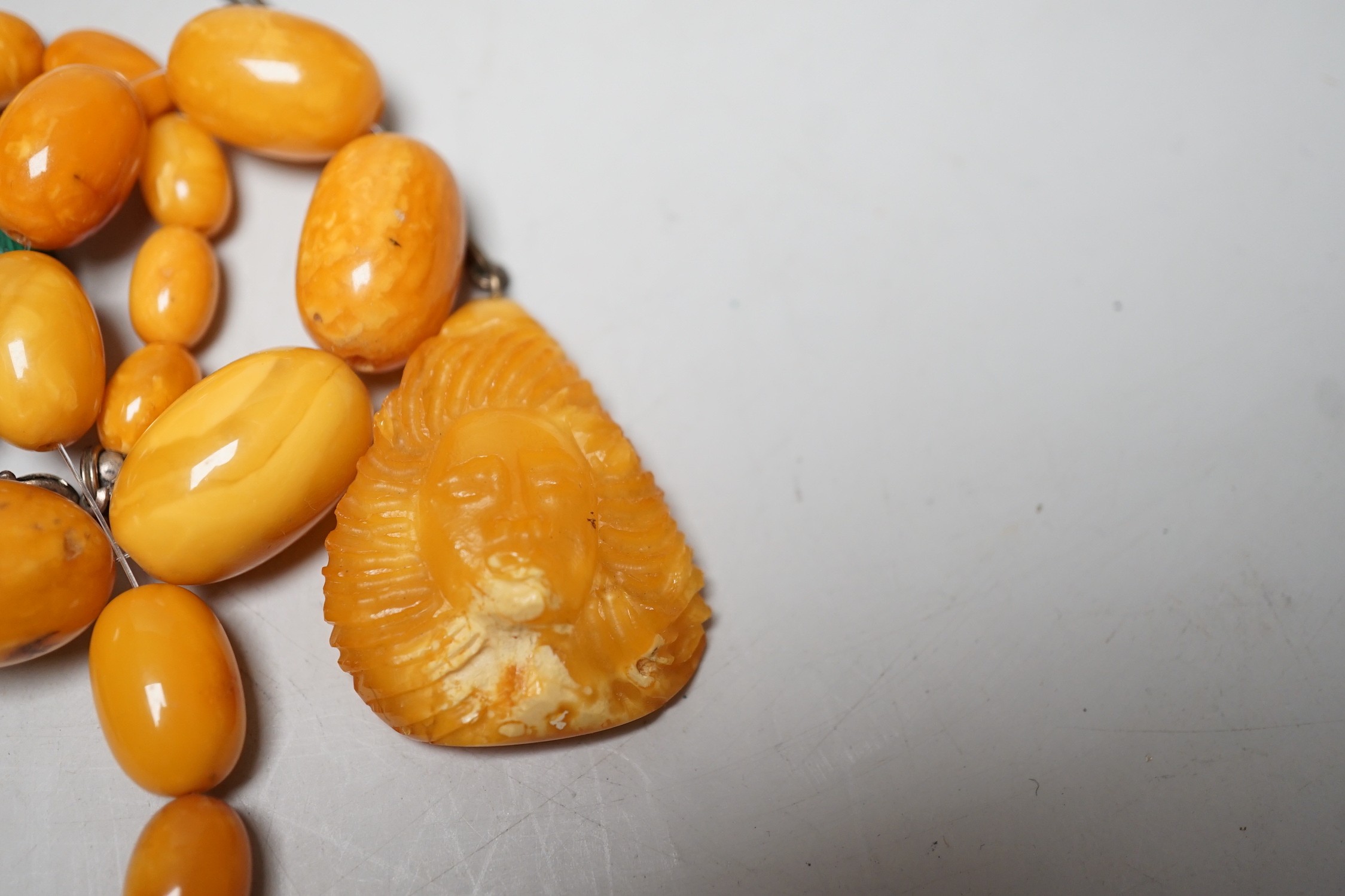 A single strand graduated amber bead necklace, a.f., 45 grams, a carved amber pendant on chain and assorted malachite beads.